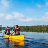 Two friends paddling in yellow canoe through calm river with green trees in distance on shoreline