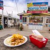 Plate of seafood plus sauces and utensils sitting on table in front of walk-up waterfront seafood shack