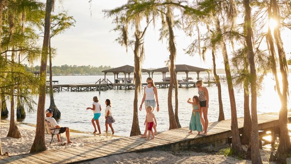 Family walking in from dock onto beach with pier and sun in background