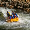 Four people on raft going down whitewaters with rocks in background