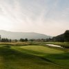 Empty golf course with clubhouse, trees and mountains in distance during daytime