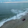 Red jeep driving on sand alongside ocean