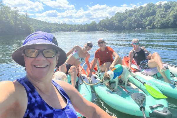 Woman taking selfie with three friends and a dog in kayaks on mountain lake