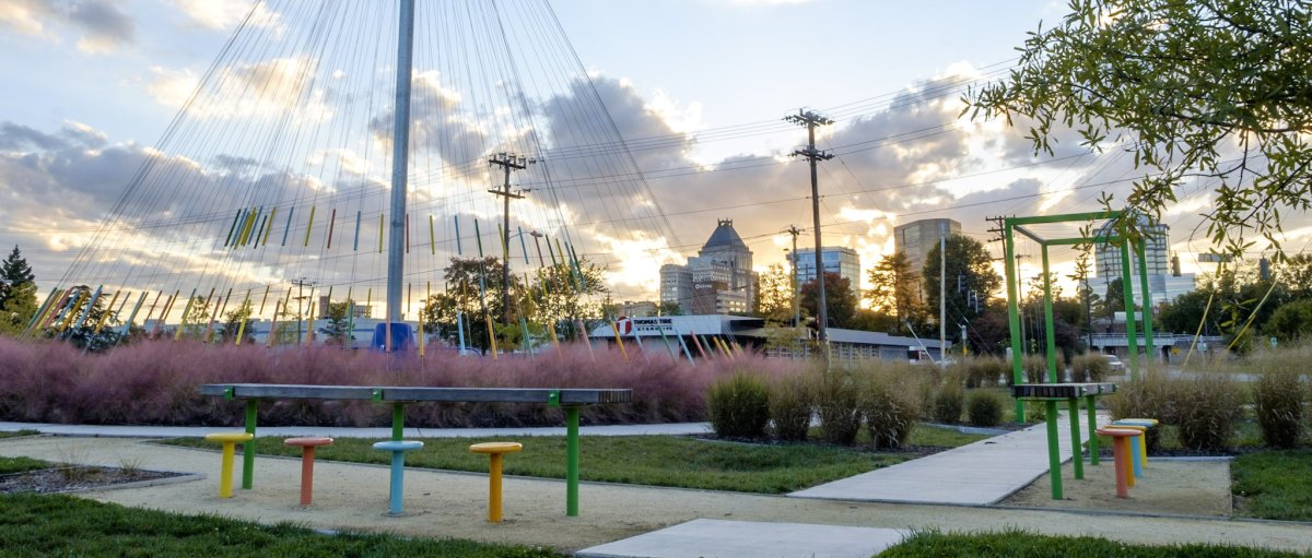 Urban park with colorful public art surrounding sidewalk with downtown Greensboro in background